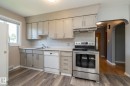 Bright kitchen featuring cream cabinetry, stainless steel appliances including a convection oven and dishwasher, white subway tile backsplash, and wood-finish flooring throughout - 12322 94 Street Nw, Edmonton, AB  - Indoor Photo Showing Kitchen 