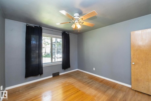 Wood-finish flooring, ceiling fan with integrated lighting, window with white trim, and a wood-finish door - 12322 94 Street Nw, Edmonton, AB - Indoor Photo Showing Other Room