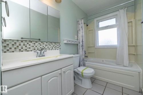 Vanity with white cabinetry and integrated sink, mosaic tile backsplash, mirrored medicine cabinet, and a bathtub with shower fixture - 12322 94 Street Nw, Edmonton, AB - Indoor Photo Showing Bathroom