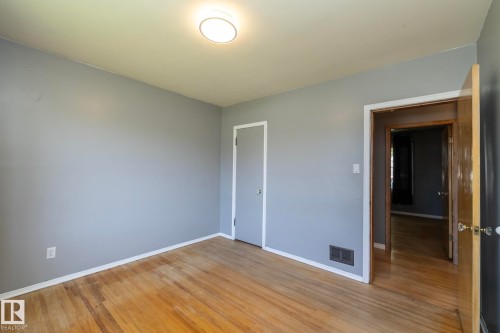 Wood-finish flooring, light gray walls, built-in closet with white trim, recessed lighting, and a solid wood door - 12322 94 Street Nw, Edmonton, AB - Indoor Photo Showing Other Room