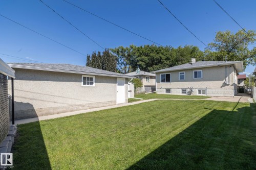 Expansive grass lawn with mature trees, a detached garage featuring a window and side door, and a concrete driveway - 12322 94 Street Nw, Edmonton, AB - Outdoor