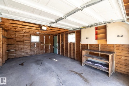 Attached garage with wood plank walls, built-in shelving, two windows, and overhead storage cabinetry - 12322 94 Street Nw, Edmonton, AB - Indoor Photo Showing Garage