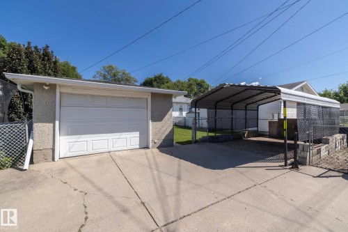 Detached garage with white panel door and an adjacent carport - 12322 94 Street Nw, Edmonton, AB - Outdoor With Exterior
