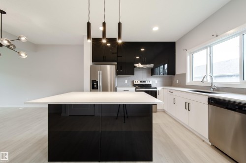 Modern kitchen featuring a white countertop island, black and white cabinetry, stainless steel appliances, and wood-finish flooring - 7109 Chivers Close Sw, Edmonton, AB - Indoor Photo Showing Kitchen With Stainless Steel Kitchen With Upgraded Kitchen