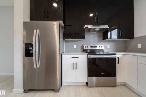 Stainless steel refrigerator with a side-by-side door, sleek black upper cabinetry, white base cabinetry, gray subway tile backsplash, and a stainless steel electric range - 7109 Chivers Close Sw, Edmonton, AB - Indoor Photo Showing Kitchen With Stainless Steel Kitchen