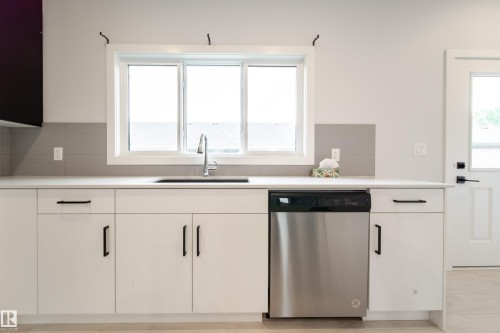 Modern kitchen featuring white cabinetry with black hardware, stainless steel dishwasher, undermount sink, and a large window - 7109 Chivers Close Sw, Edmonton, AB - Indoor Photo Showing Kitchen