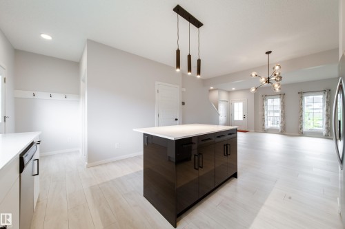 Central kitchen island with glossy dark cabinetry and white countertop - 7109 Chivers Close Sw, Edmonton, AB - Indoor Photo Showing Kitchen