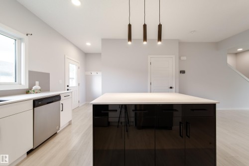 Kitchen with a large island featuring a light-toned countertop and dark, high-gloss cabinetry - 7109 Chivers Close Sw, Edmonton, AB - Indoor Photo Showing Kitchen
