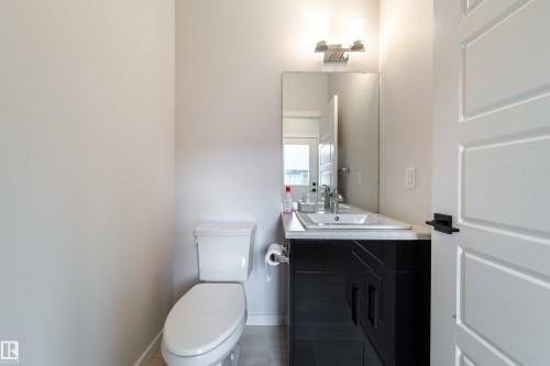 White paneled door with black hardware, black vanity with white countertop, undermount sink, wall-mounted mirror, and a two-light vanity fixture - 7109 Chivers Close Sw, Edmonton, AB - Indoor Photo Showing Bathroom