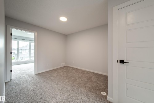 Recessed ceiling lighting, light gray carpet flooring, white interior trim, white paneled door with matte black hardware, and an open doorway - 7109 Chivers Close Sw, Edmonton, AB - Indoor Photo Showing Other Room