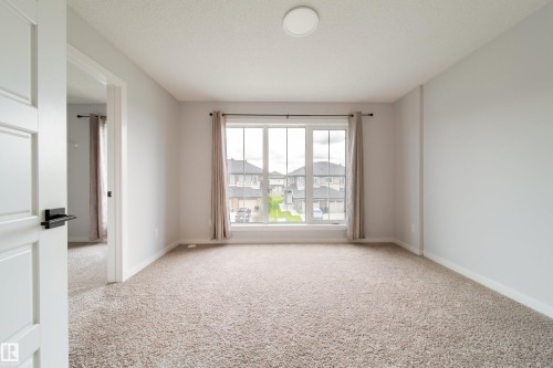 Bright corner bedroom showcasing neutral carpet flooring, expansive windows with rod-pocket drapery, and abundant natural light - 7109 Chivers Close Sw, Edmonton, AB - Indoor Photo Showing Other Room