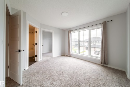 Carpeted room with a large multi-pane window, white trim, and a flush-mount ceiling light - 7109 Chivers Close Sw, Edmonton, AB - Indoor Photo Showing Other Room