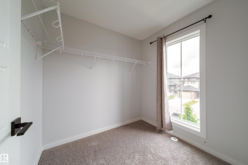 Neutral wall color, carpeted flooring, large window with white frame, closet shelving, and a dark-finish door handle - 7109 Chivers Close Sw, Edmonton, AB - Indoor