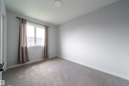 Neutral wall palette, window with white trim, gray carpet, and ceiling-mounted light fixture - 7109 Chivers Close Sw, Edmonton, AB - Indoor Photo Showing Other Room