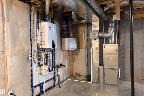 Tankless water heater, furnace system, whole-house humidifier, exposed ceiling ductwork, and concrete flooring - 7109 Chivers Close Sw, Edmonton, AB - Indoor Photo Showing Basement