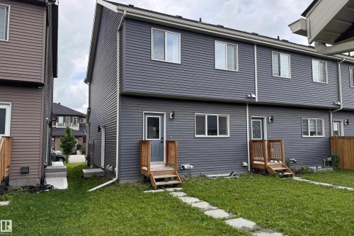 Gray siding exterior with multiple windows, two exterior doors with wood steps, and a grass lawn with stepping stones - 7109 Chivers Close Sw, Edmonton, AB - Outdoor