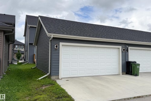 Exterior featuring dark gray siding, a white panel garage door, concrete driveway, and black roofing - 7109 Chivers Close Sw, Edmonton, AB - Outdoor With Exterior