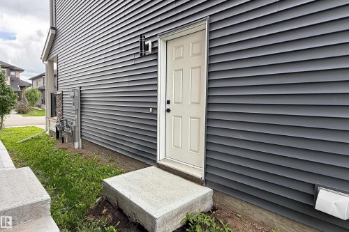 Dark gray horizontal siding, white paneled door, and concrete steps - 7109 Chivers Close Sw, Edmonton, AB - Outdoor