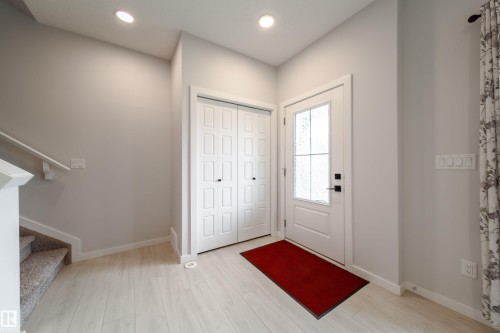 Light wood-finish flooring, white paneled closet doors, and a white front door with decorative glass - 7109 Chivers Close Sw, Edmonton, AB - Indoor Photo Showing Other Room
