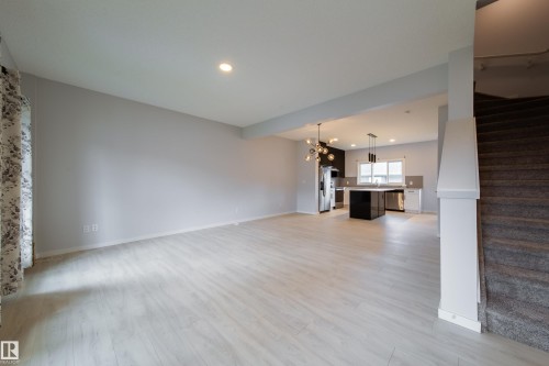 Spacious living area featuring light wood-finish flooring, recessed lighting, and a kitchen with a dark island, stainless steel appliances, and pendant lighting - 7109 Chivers Close Sw, Edmonton, AB - Indoor