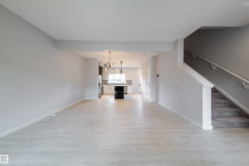 Open-concept living area featuring wood-finish flooring, a modern chandelier, and a carpeted staircase with a white railing - 7109 Chivers Close Sw, Edmonton, AB - Indoor