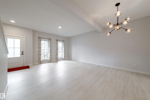 White wood-finish flooring, two large windows, recessed ceiling lighting, and a contemporary chandelier - 7109 Chivers Close Sw, Edmonton, AB - Indoor