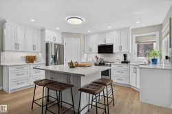 White shaker-style cabinetry, stainless steel appliances, light wood-finish flooring, recessed lighting, and a kitchen island with seating - 
