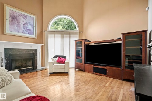 Living area featuring vaulted ceilings, wood-finish flooring, a fireplace with a white mantel and dark stone surround, and an arched window with panel blinds - #25 3811 85 St Nw, Edmonton, AB - Indoor Photo Showing Living Room With Fireplace
