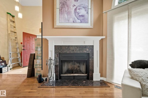 Hardwood flooring, fireplace with stone surround and white mantel, natural light, and panel track window treatments - #25 3811 85 St Nw, Edmonton, AB - Indoor Photo Showing Living Room With Fireplace