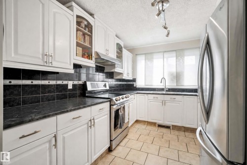 White cabinetry, black tile backsplash, stainless steel appliances, dark countertops, and tiled flooring - #25 3811 85 St Nw, Edmonton, AB - Indoor Photo Showing Kitchen With Upgraded Kitchen
