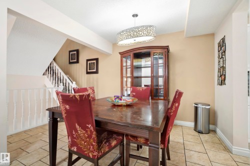 Dining area featuring large format tile flooring, a decorative chandelier, and a wood staircase with white balusters - #25 3811 85 St Nw, Edmonton, AB - Indoor Photo Showing Dining Room