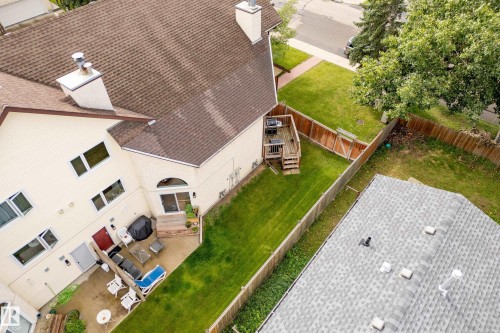 Expansive property featuring a brown shingle roof, light-colored siding, a wooden deck, a patio, and a grass lawn - #25 3811 85 St Nw, Edmonton, AB - Outdoor