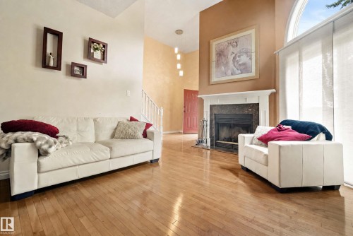 Hardwood flooring throughout, a fireplace with a stone surround and white mantle, and a large arched window with panel blinds - #25 3811 85 St Nw, Edmonton, AB - Indoor Photo Showing Living Room With Fireplace