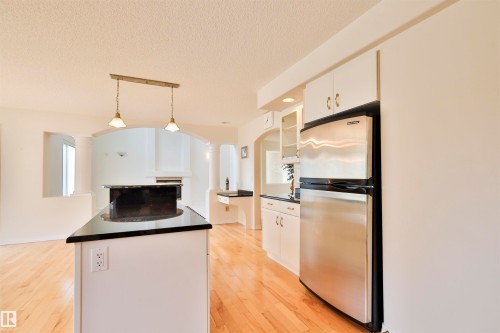 Kitchen with light wood flooring, white cabinetry, stainless steel refrigerator, and a kitchen island featuring a black countertop - 237 Darlington Crescent Nw, Edmonton, AB - Indoor Photo Showing Kitchen