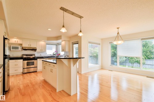 Hardwood flooring throughout, white cabinetry with dark countertops, stainless steel appliances, and multiple windows - 237 Darlington Crescent Nw, Edmonton, AB - Indoor Photo Showing Kitchen