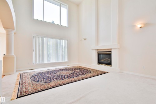 Sizable living area with high ceilings, featuring a built-in fireplace with a hearth, multiple windows, and a decorative column - 237 Darlington Crescent Nw, Edmonton, AB - Indoor With Fireplace
