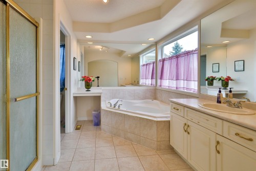 Tile flooring with a corner soaking tub, a single vanity with an integrated sink, and an enclosed shower with a gold-finish frame - 237 Darlington Crescent Nw, Edmonton, AB - Indoor Photo Showing Bathroom