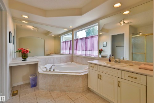 Recessed lighting illuminates a built-in corner soaking tub with tile surround, a spacious vanity with an integrated sink, and an expansive wall-mounted mirror - 237 Darlington Crescent Nw, Edmonton, AB - Indoor Photo Showing Bathroom
