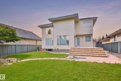 Rear exterior featuring stucco finish, multiple windows, a rear entry door, and a brick paver patio with tiered steps - 237 Darlington Crescent Nw, Edmonton, AB - Outdoor