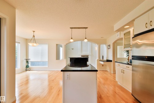 Spacious interior featuring wood-finish flooring, a kitchen island with pendant lighting, white cabinetry with brass hardware, stainless steel appliances, and arched doorways - 237 Darlington Crescent Nw, Edmonton, AB - Indoor Photo Showing Kitchen