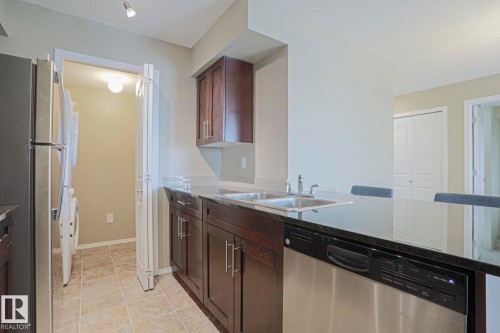 Kitchen featuring wood-finish cabinetry, stainless steel dishwasher, double basin sink, and stone-finish countertops - #321 270 Mcconachie Dr Nw, Edmonton, AB - Indoor Photo Showing Kitchen With Double Sink