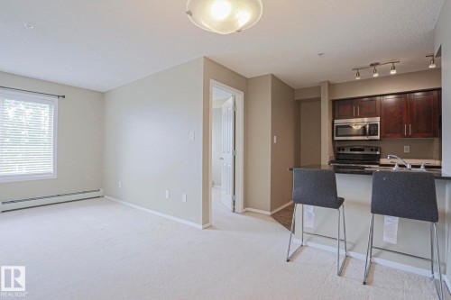 Open concept layout with carpeting, window with blinds, and dark wood-finish kitchen cabinetry - #321 270 Mcconachie Dr Nw, Edmonton, AB - Indoor Photo Showing Kitchen