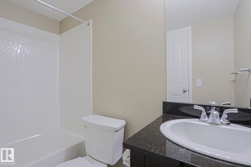 Bathroom featuring a tub/shower combination with white tile surround, a vanity with a dark countertop and integrated sink, a chrome faucet, and a wall-mounted mirror - #321 270 Mcconachie Dr Nw, Edmonton, AB - Indoor Photo Showing Bathroom