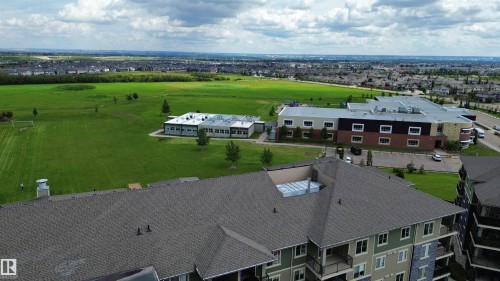 Expansive green space and a multi-story building featuring a facade with multiple window configurations - #321 270 Mcconachie Dr Nw, Edmonton, AB - Outdoor With View