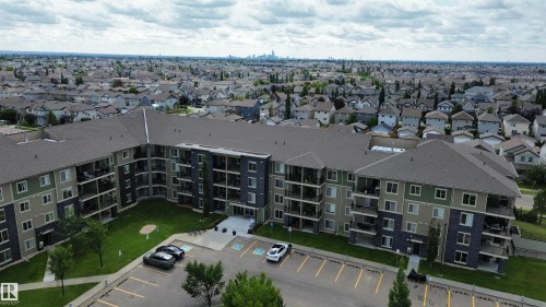 Multi-story building featuring multiple private balconies, a central courtyard with manicured lawn, and an adjacent paved parking area - #321 270 Mcconachie Dr Nw, Edmonton, AB - Outdoor With View