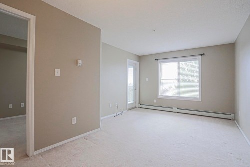 Neutral-toned walls, light-colored carpet flooring, white window blinds, and white trim throughout - #321 270 Mcconachie Dr Nw, Edmonton, AB - Indoor Photo Showing Other Room