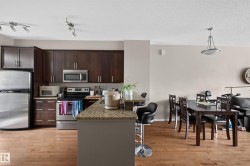 Open-concept kitchen and dining area featuring wood-finish flooring, dark wood cabinetry, stainless steel appliances, and track lighting - 