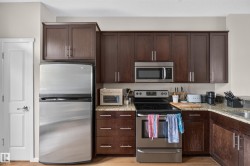 Kitchen featuring dark wood-finish cabinetry, stainless steel appliances, speckled stone countertops, and a gray tile backsplash - 