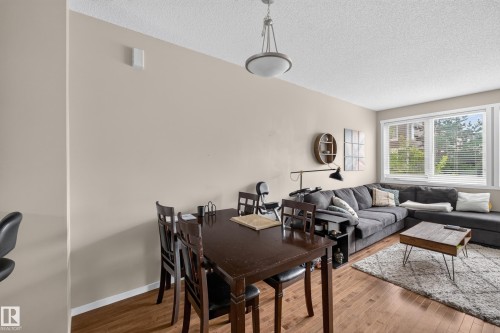 Open-concept living area featuring wood-finish flooring, a large multi-pane window with blinds, and neutral wall tones - #53 603 Watt Bv Sw, Edmonton, AB - Indoor Photo Showing Living Room