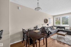 Open-concept living area featuring wood-finish flooring, a large multi-pane window with blinds, and neutral wall tones - 